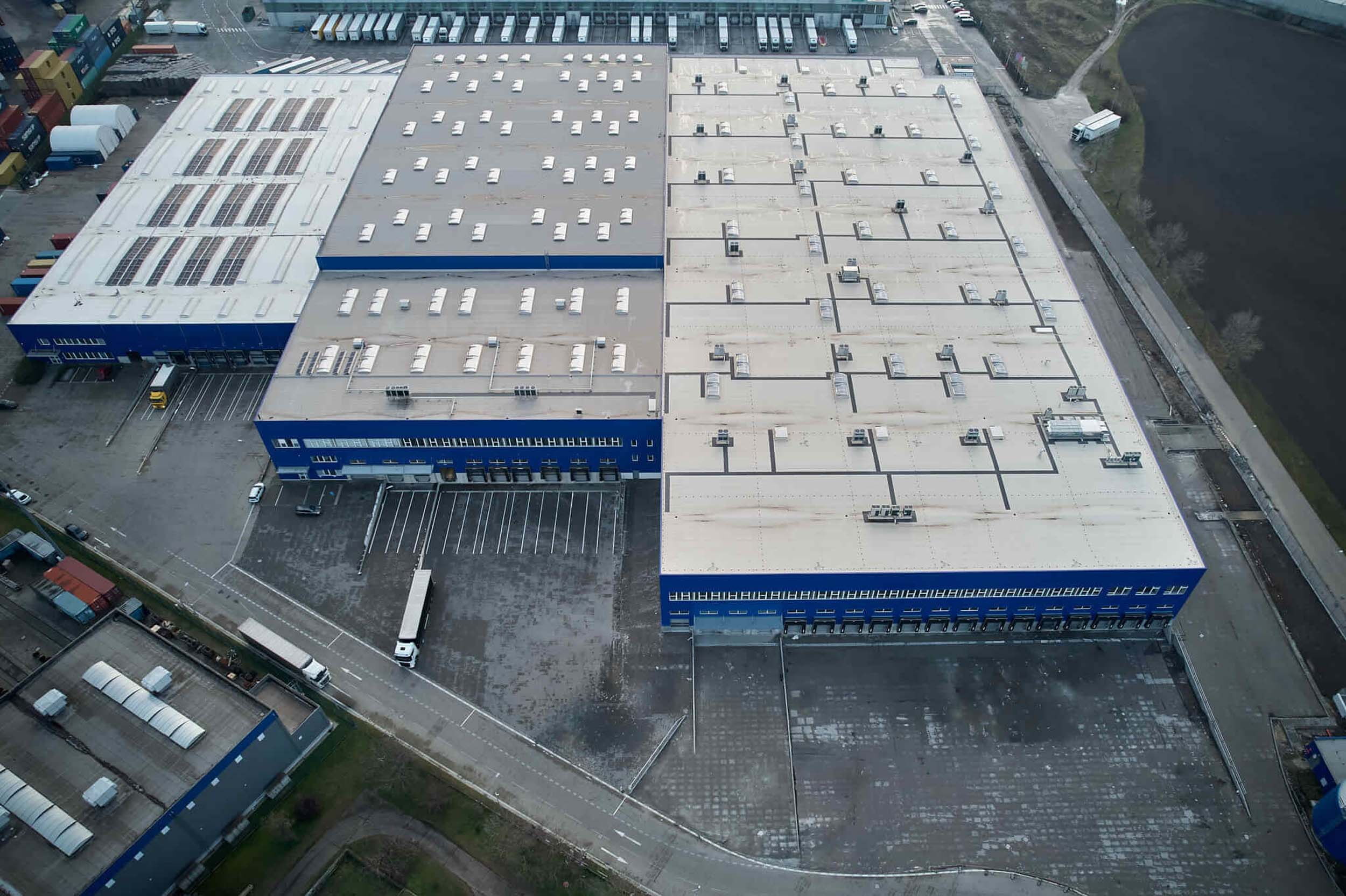 Aerial view of a large logistics warehouse with blue buildings and trucks