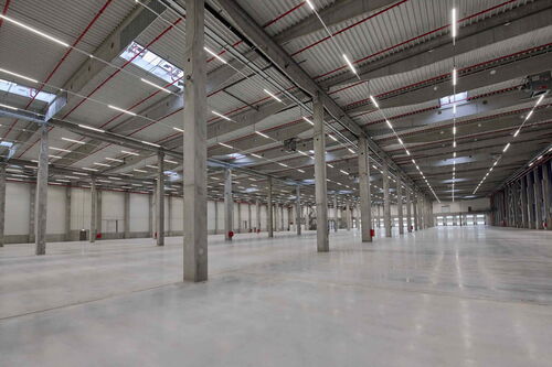 Interior view of a large, empty, and modern warehouse with concrete flooring and high ceilings
