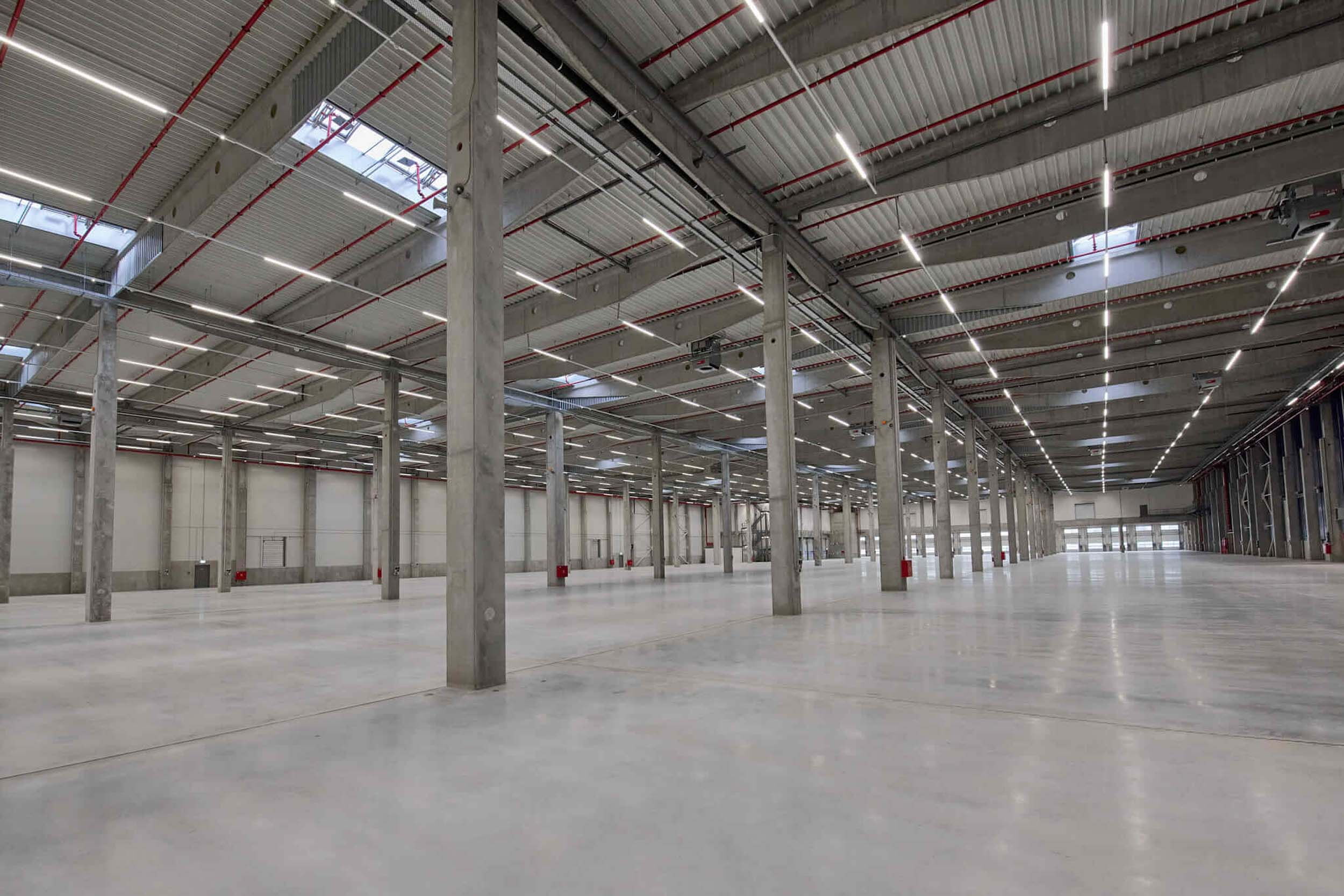 Interior view of a large, empty, and modern warehouse with concrete flooring and high ceilings